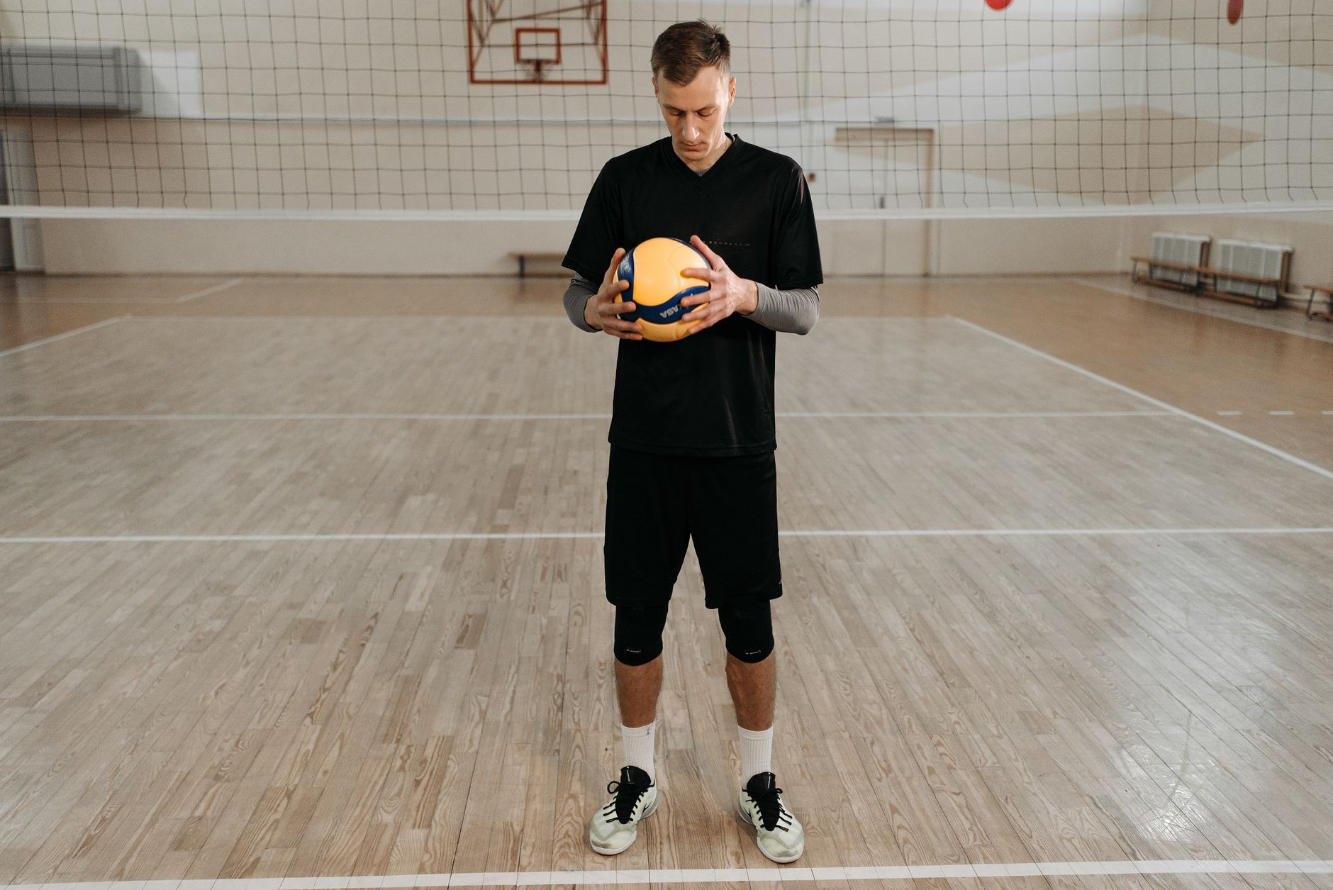 Siatkarz w czarnym stroju stoi z piłką na hali sportowej