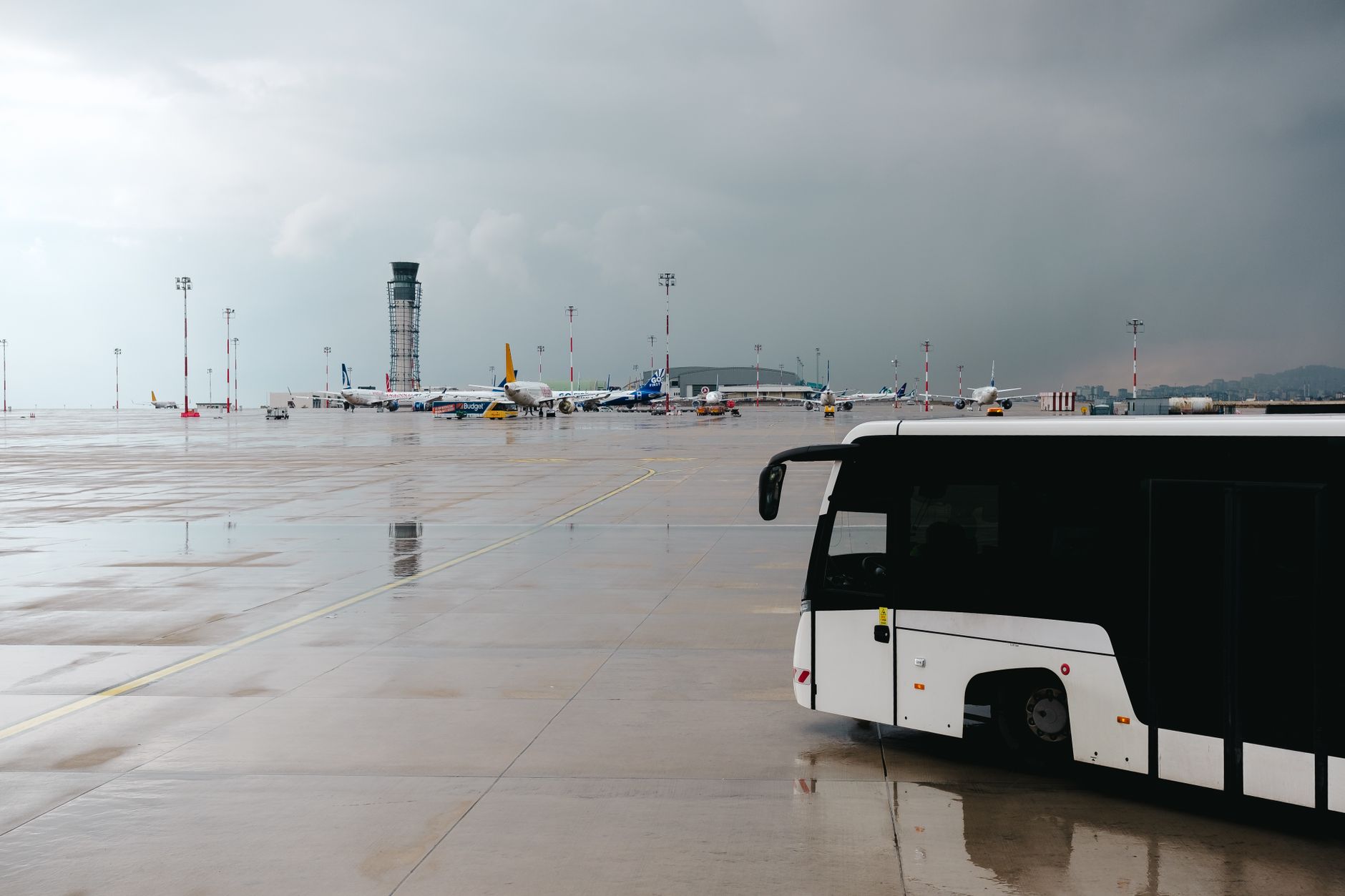 Autobus pasażerski na mokrej płycie lotniska, w tle samoloty